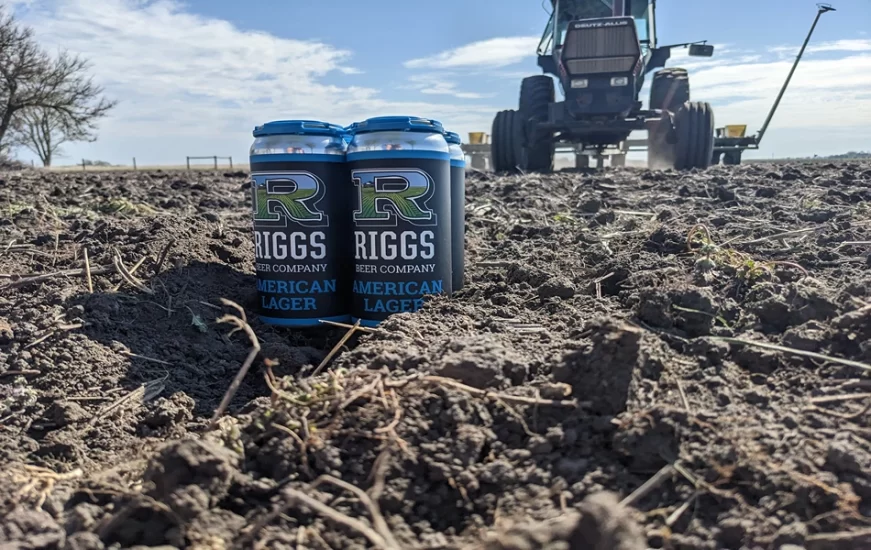 Riggs Beer Company_A four pack of American Lager sitting in front the tractor that's planting next year's crop photo credit Matt Riggs