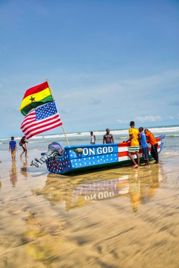 A Group of People Standing next to a Boat with a Flag of Ghana and the United States